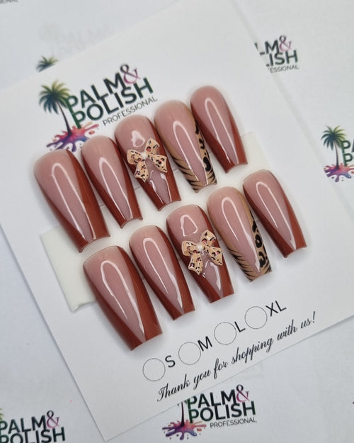 A set of artificial press-on nails displayed on a white card, featuring a nude pink base with a diagonal metallic gold glitter stripe and a small gold floral accent near the tip. The nails are laid flat on a white background patterned with the 'Balm & Polish' brand logo.
