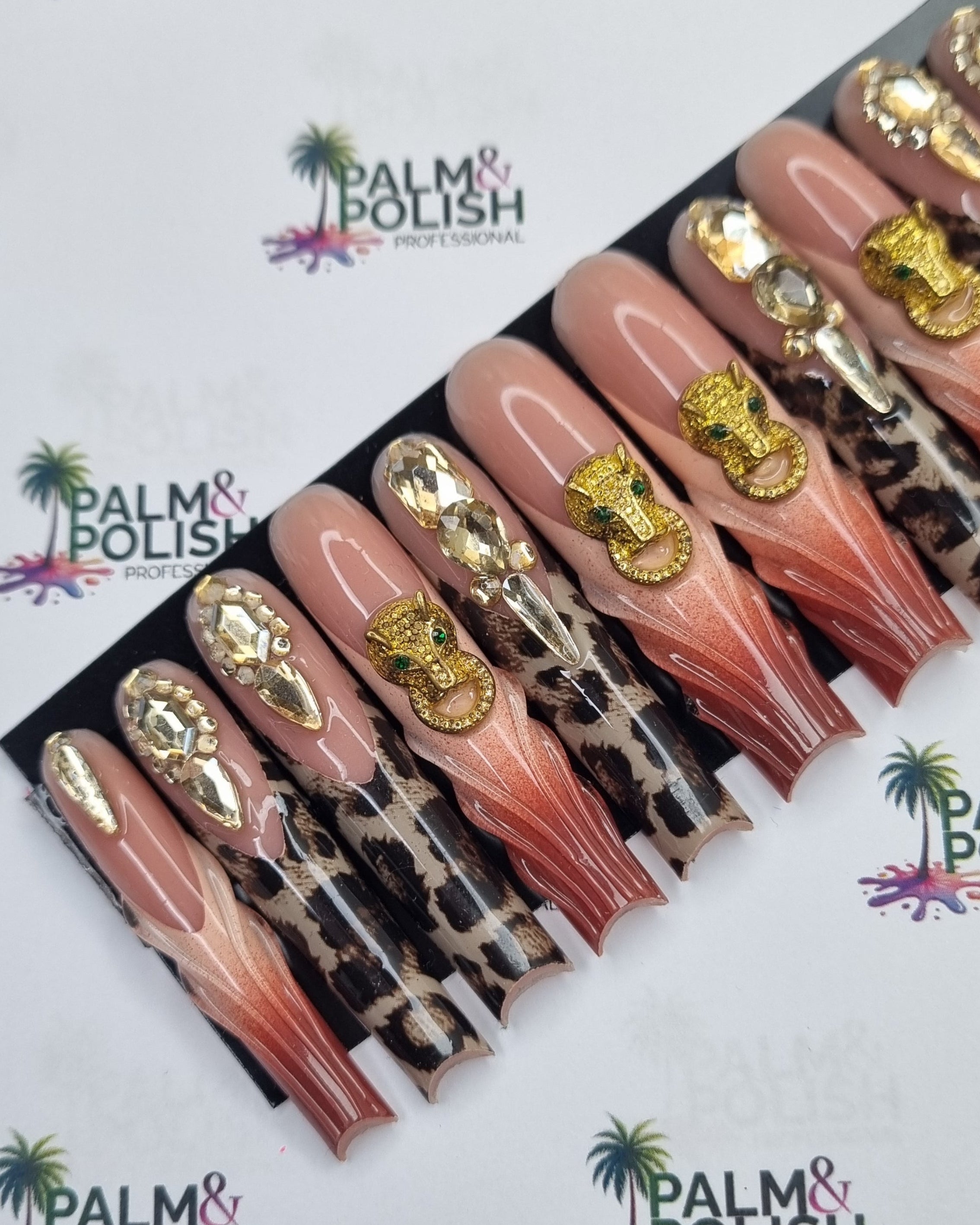 A set of false press-on nails displayed on a black card, featuring a gradient from pink to nude with gold glitter and rhinestone embellishments, set against a white background printed with the Palm & Polish brand logo.