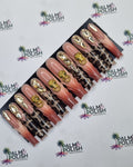 A set of false press-on nails displayed on a black card, featuring a gradient from pink to nude with leopard print and gold foil accents, set against a white background with a repeating Palm & Polish logo.