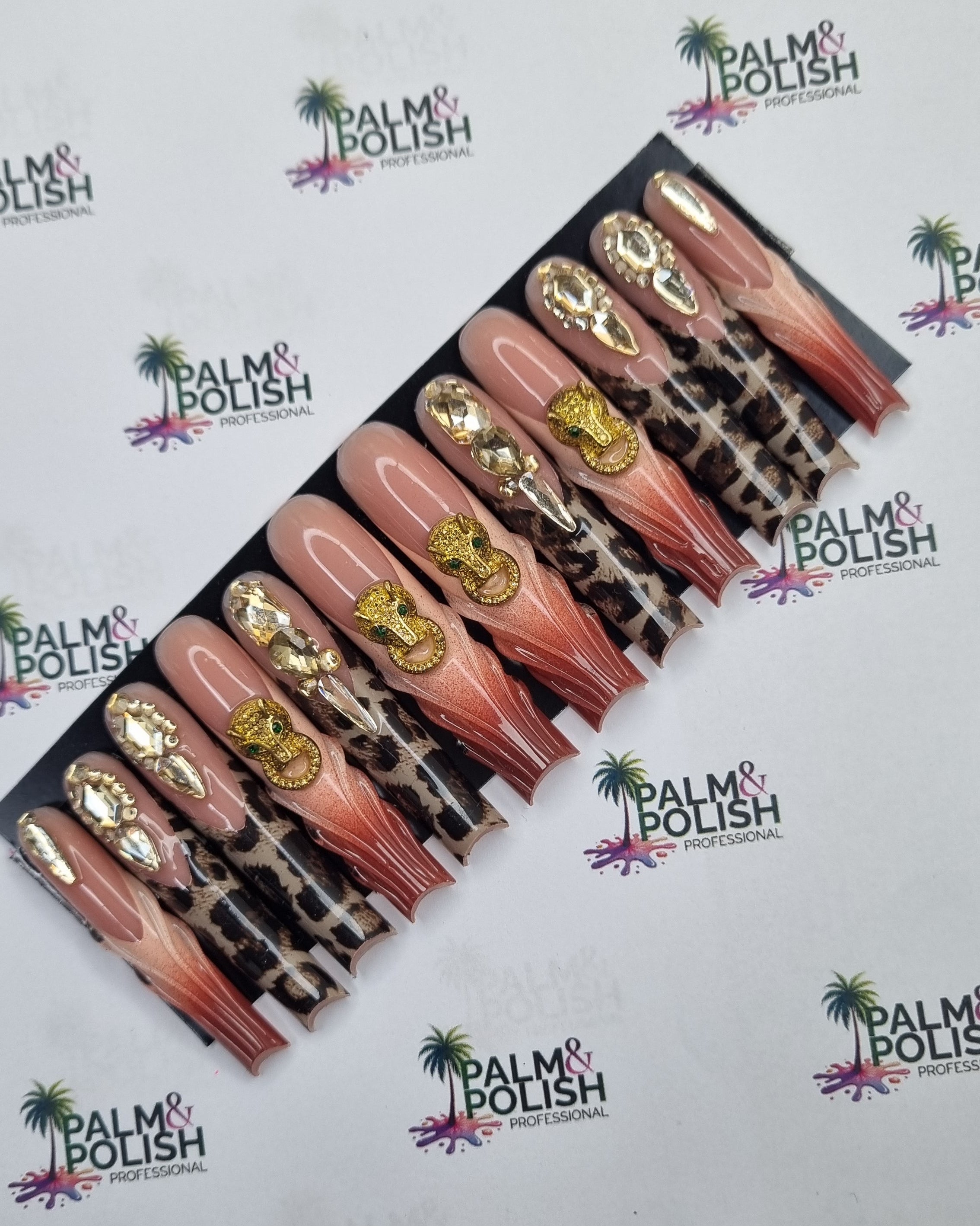 A set of false press-on nails displayed on a black card, featuring a gradient from pink to nude with leopard print and gold foil accents, set against a white background with a repeating Palm & Polish logo.