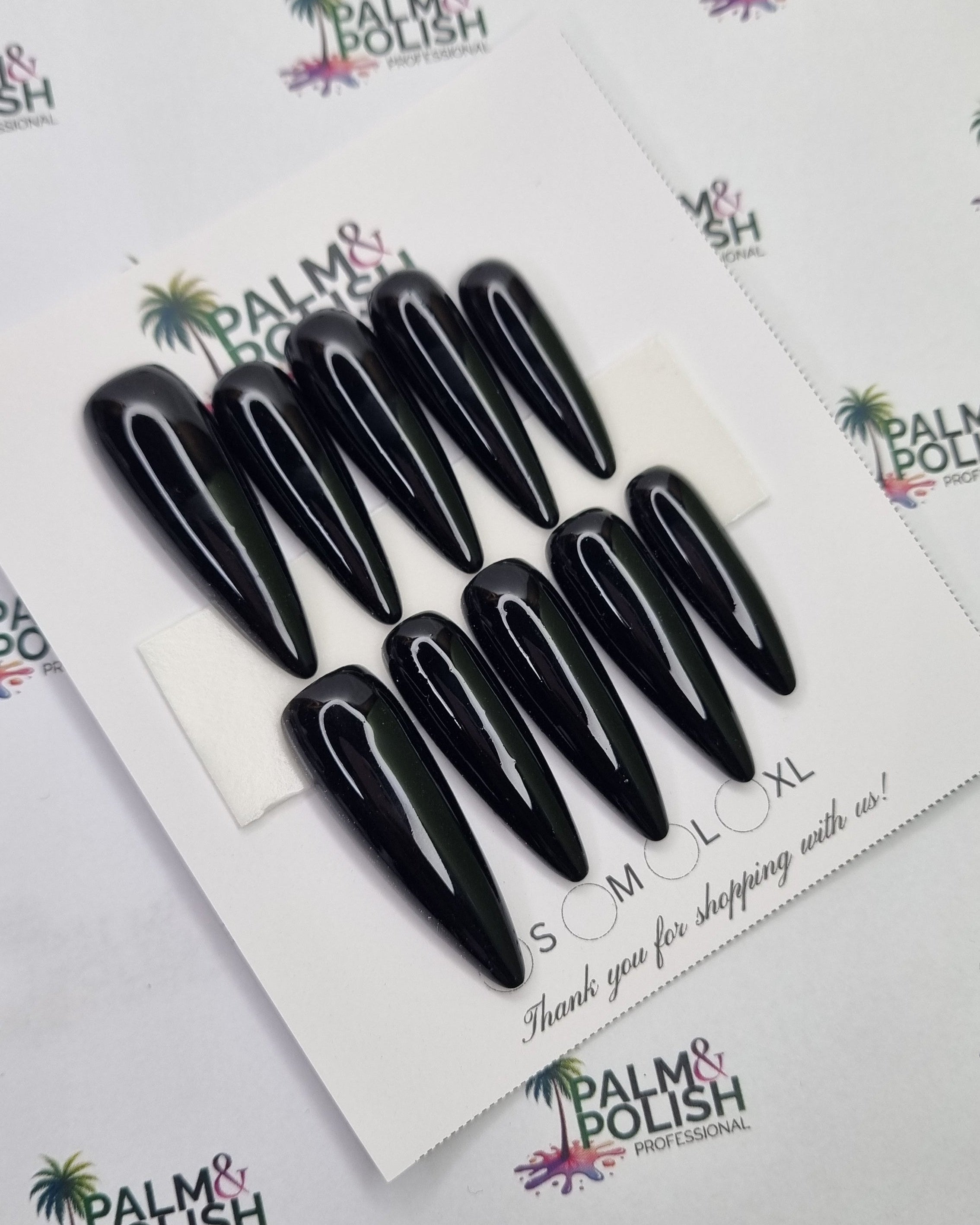Ten black 2xl stiletto presson nail arranged on a white display card, photographed from above on a white background with Palm & Polish branding.