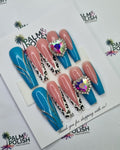 A set of acrylic press-on nails displayed on a white card, featuring pastel pink, bright blue, and leopard-print designs with rhinestone embellishments. The card is placed on a white background printed with the 'palm & Polish' brand logo.