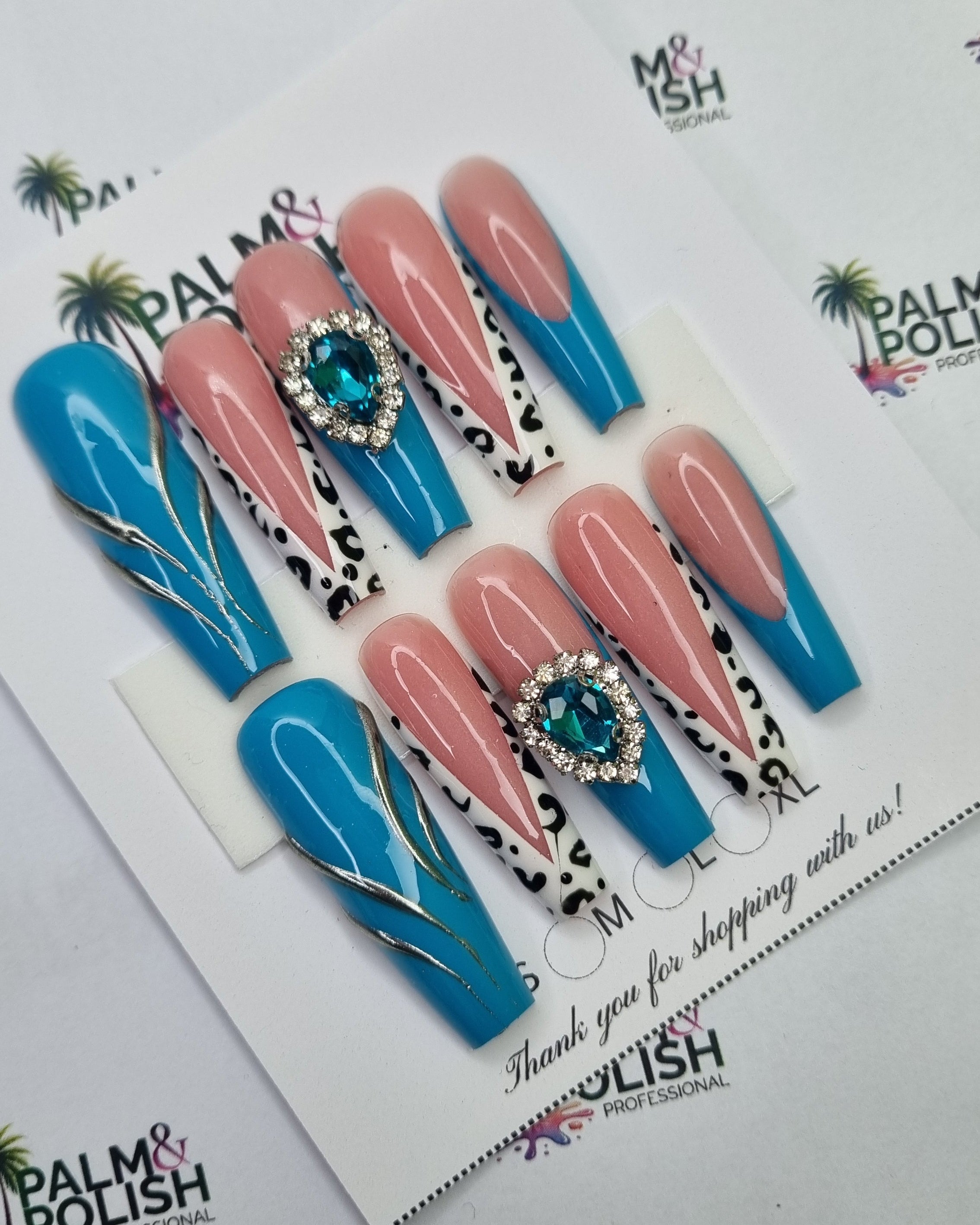 A set of acrylic press-on nails displayed on a white card, featuring a mix of solid blue, pink with leopard print, and blue with gold leaf designs, with rhinestone accents. The background is a white surface printed with the Palm & Polish Professional logo.
