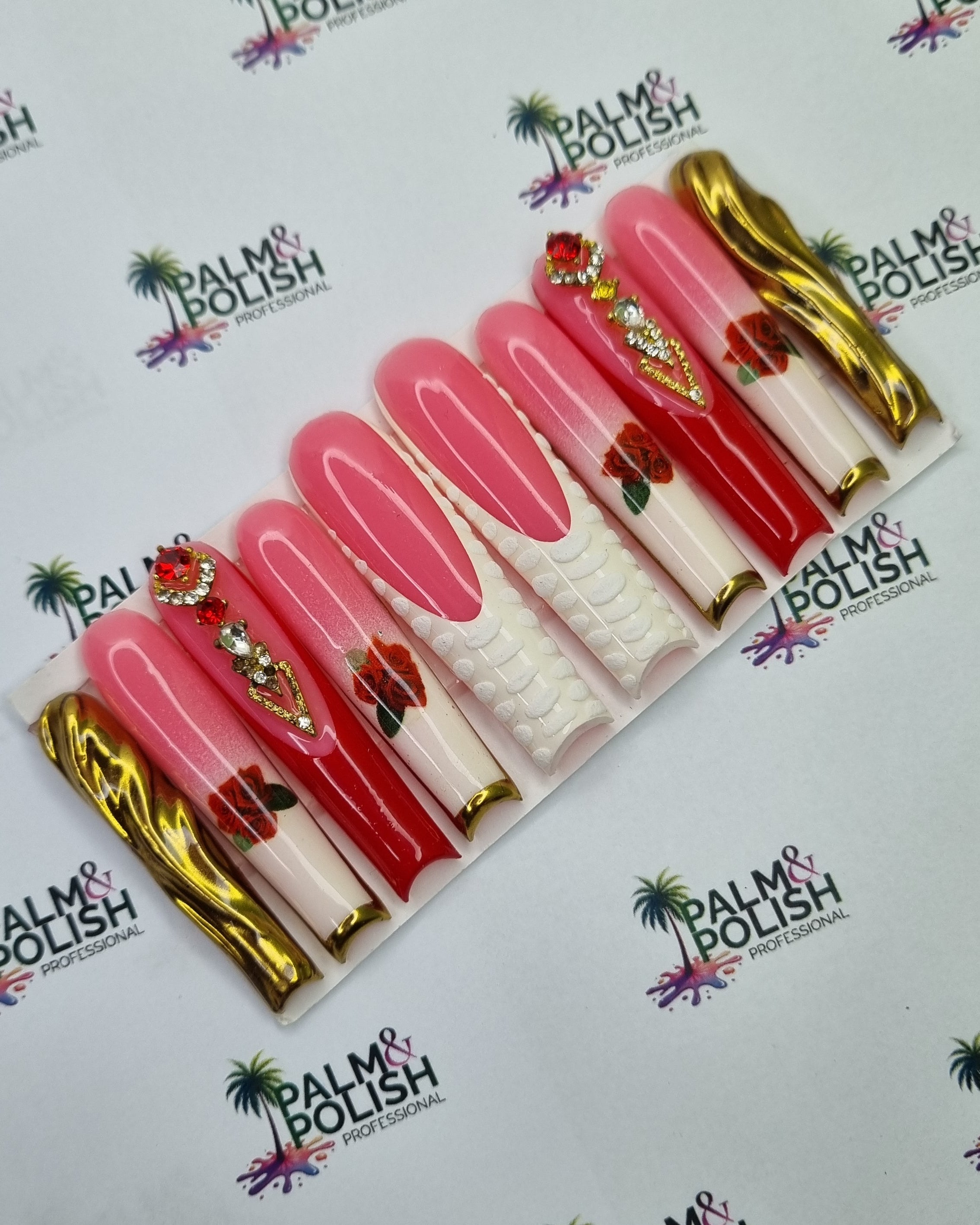 A set of jamaica acrylic press-on nails displayed on a white backing card, featuring pink and red gradient designs with gold glitter accents, floral details, and white textured tips. The card is placed on a white background printed with the 'rose' brand logo.