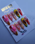 A set of colorful press-on nails displayed on a white card labeled 'Acrylic Press-On Nail vendor,' placed on a white plate.
