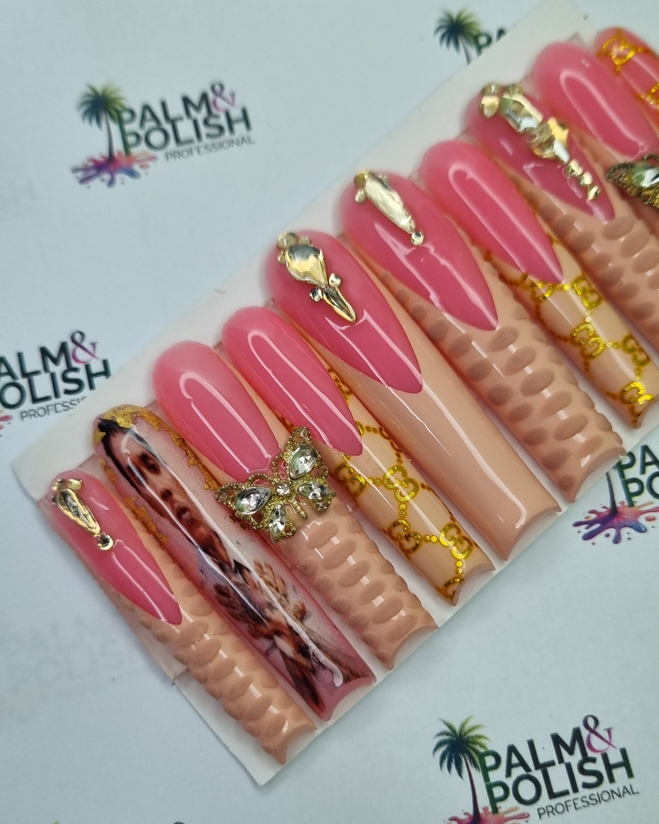 A set of acrylic press-on nails displayed on a white backing card, featuring pink and nude tones with gold glitter, rhinestone embellishments, and one tortoise shell-patterned nail, set against a branded white background.